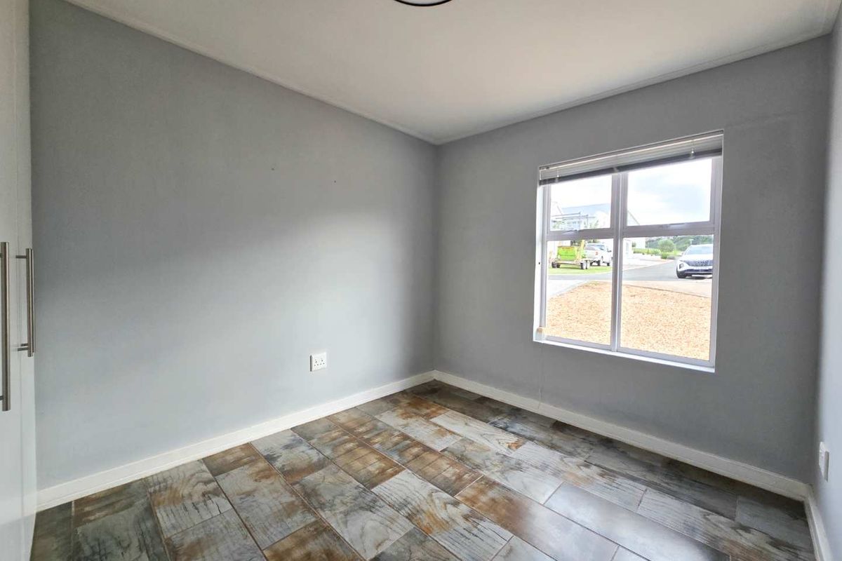 A bright, empty bedroom featuring modern wood-look tile flooring, neutral grey walls, and a built-in wardrobe.