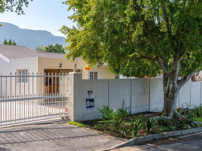 Front exterior view of the property featuring a secure gated entrance, paved driveway, and perimeter fencing with established trees.