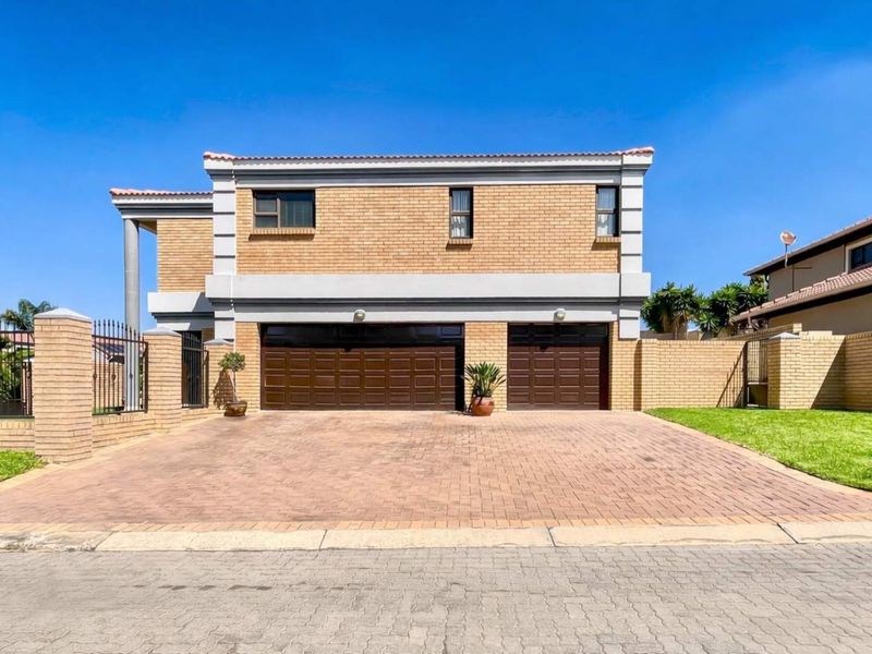 Front elevation of a double-storey cluster home featuring a double garage, paved driveway, and facebrick exterior with perimeter wall and fencing.