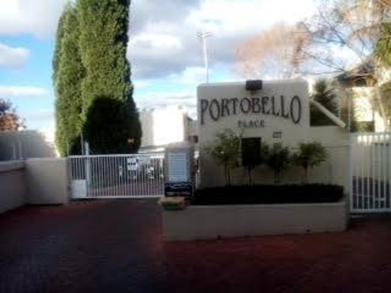 Entrance view of Portobello Place apartment complex featuring a security gate, brick paved driveway, and complex signage.