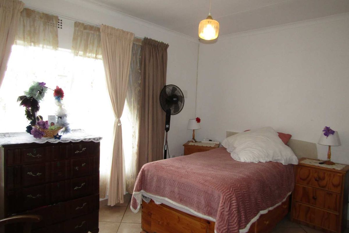 A bedroom featuring tiled flooring and a large window with curtain treatments, providing natural light to the space.