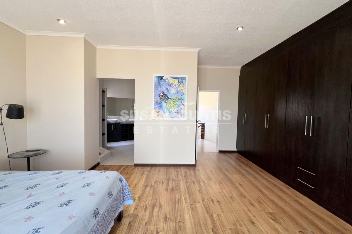 Spacious bedroom featuring dark wood-finish built-in cupboards, laminate flooring, recessed ceiling lighting, and direct access to an en-suite bathroom.