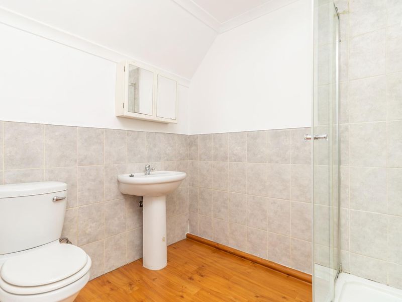 A functional bathroom featuring a pedestal basin, toilet, and a glass-enclosed shower with neutral wall tiling and laminate flooring.