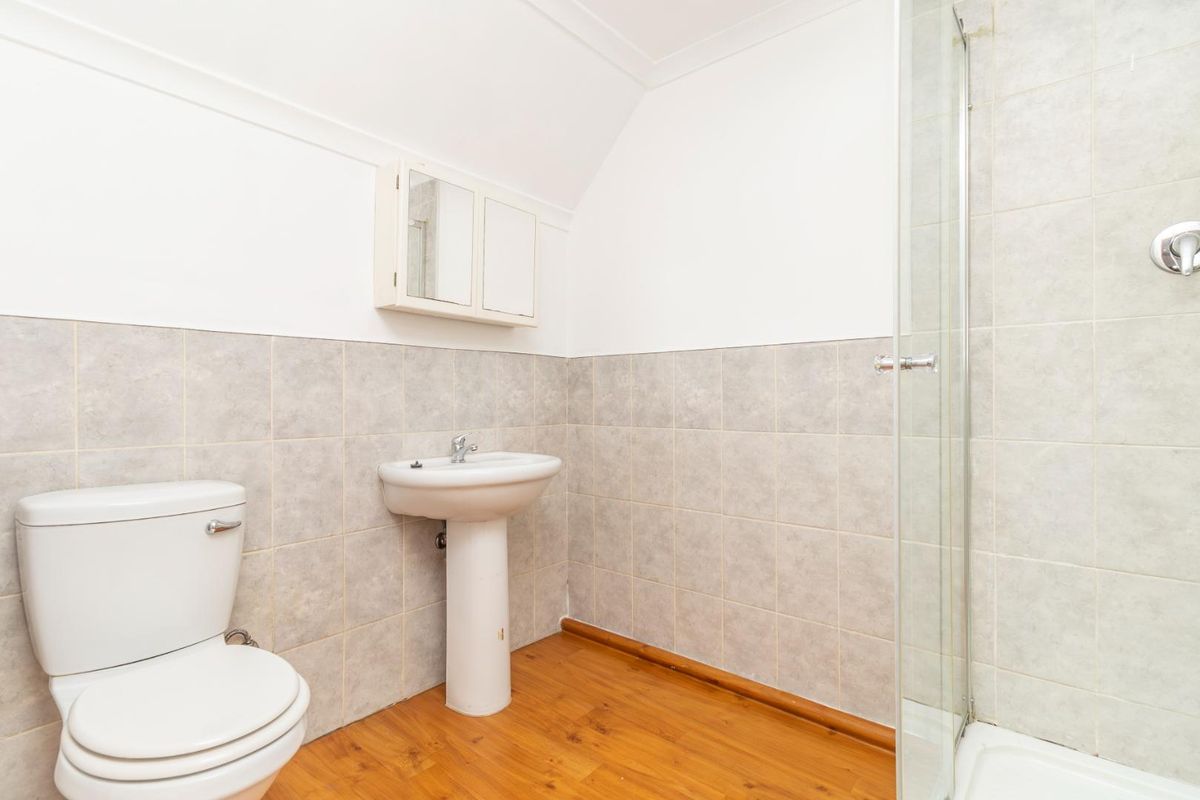 A functional bathroom featuring a pedestal basin, toilet, and a glass-enclosed shower with neutral wall tiling and laminate flooring.