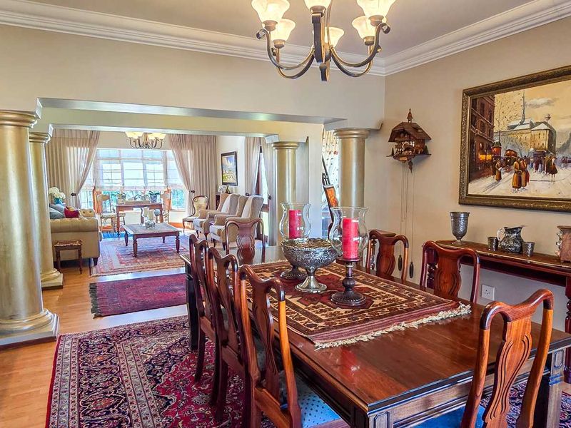 Spacious open-plan dining and living area featuring decorative columns, laminate flooring, and elegant crown molding, creating a warm and inviting atmosphere.