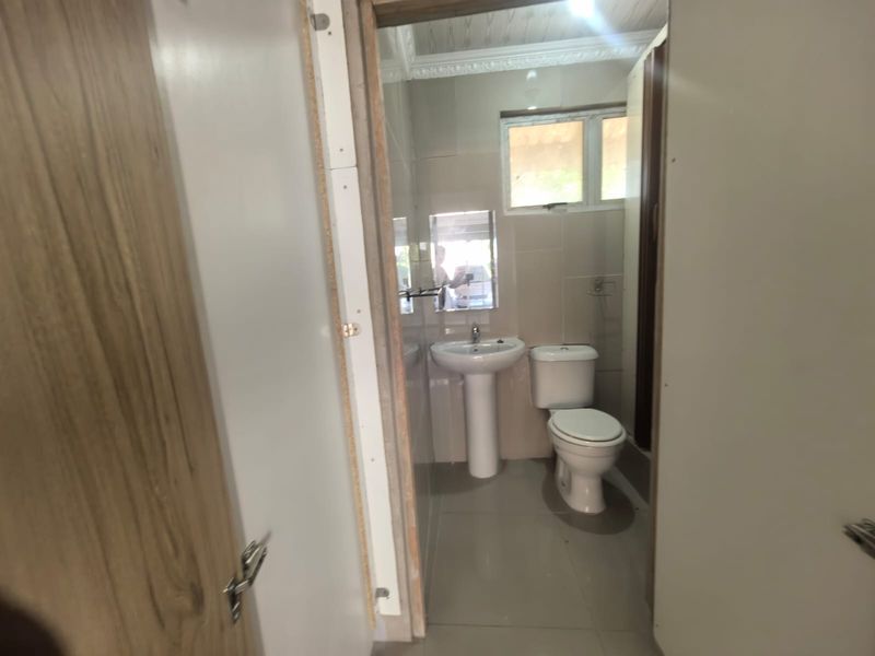 A functional bathroom featuring a pedestal basin, toilet, and tiled finishes, currently requiring finishing touches to the door frame.