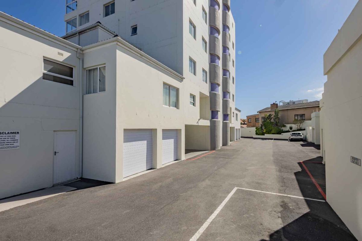 Rear exterior view of the apartment building featuring an asphalt driveway, parking area, and multiple garage access points.