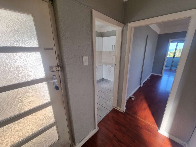 Entrance hallway featuring laminate flooring, leading to a tiled kitchen area and a bright living space with balcony access.