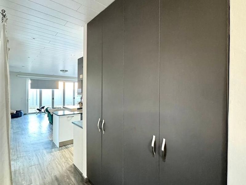 A clean, modern hallway featuring extensive floor-to-ceiling built-in cabinetry, wood-look laminate flooring, and a bright, panelled ceiling leading into an open-plan living area.