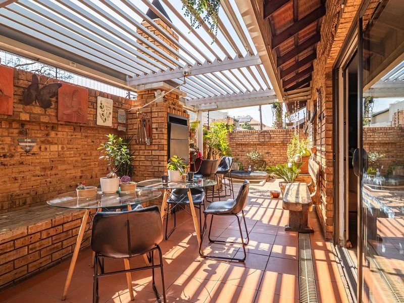 A well-maintained covered patio featuring a built-in brick braai, louvre roof system, and tiled flooring, perfect for outdoor entertaining.