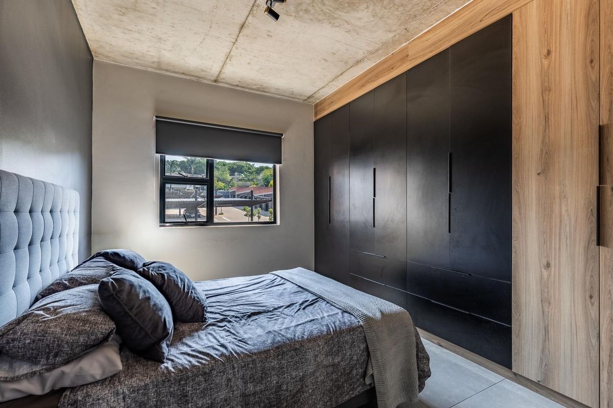 Modern bedroom featuring a raw concrete ceiling, large floor-to-ceiling built-in wardrobes with a sleek black and wood finish, and tiled flooring.