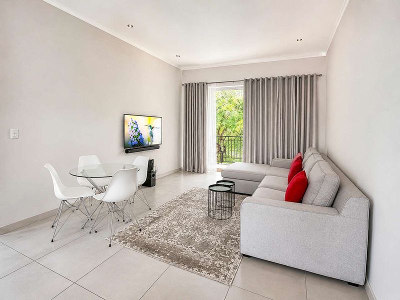 A bright and modern living room featuring neutral tiled flooring, recessed lighting, and a sliding glass door providing access to an outdoor balcony area.