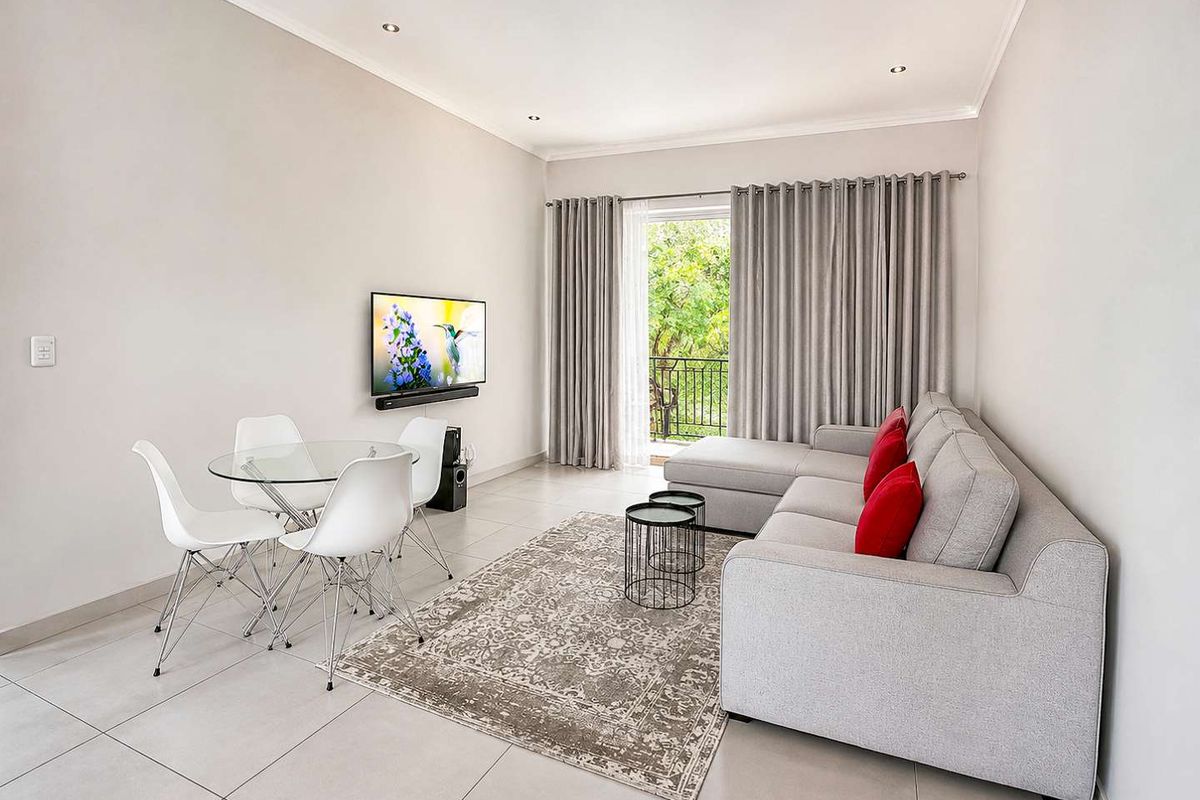 A bright and modern living room featuring neutral tiled flooring, recessed lighting, and a sliding glass door providing access to an outdoor balcony area.