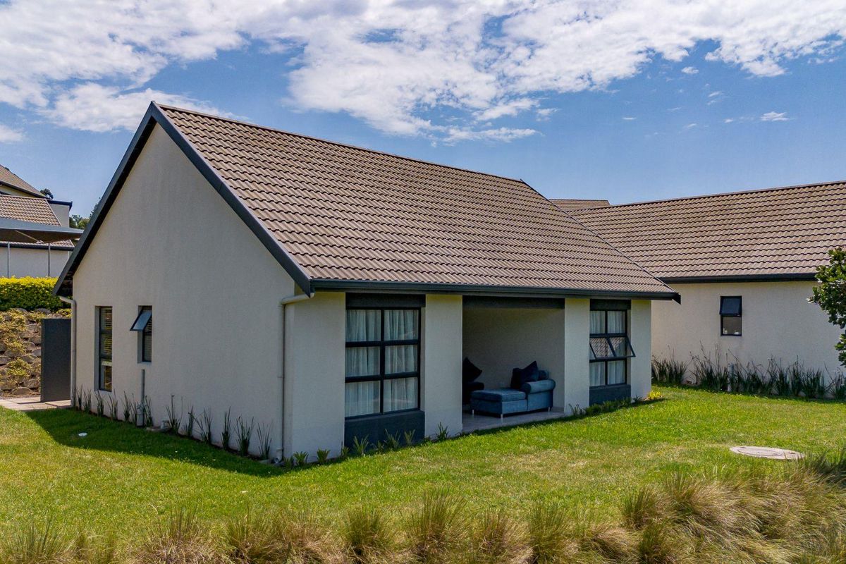 A view of the rear exterior of the townhouse, featuring a covered patio area, tiled roof, and surrounding lawn.