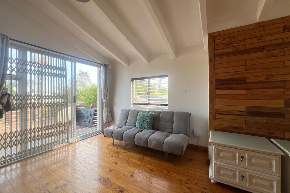 Living room featuring exposed ceiling beams, timber flooring, and a sliding door leading to an outdoor area with security gate.