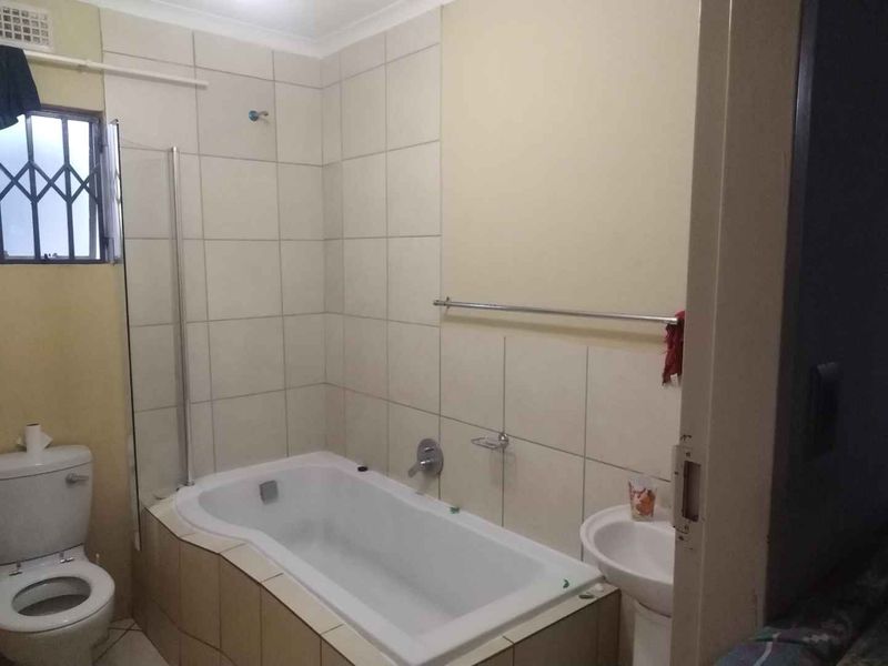A functional bathroom featuring a bathtub with a glass screen, pedestal basin, and toilet, finished with neutral wall tiling.