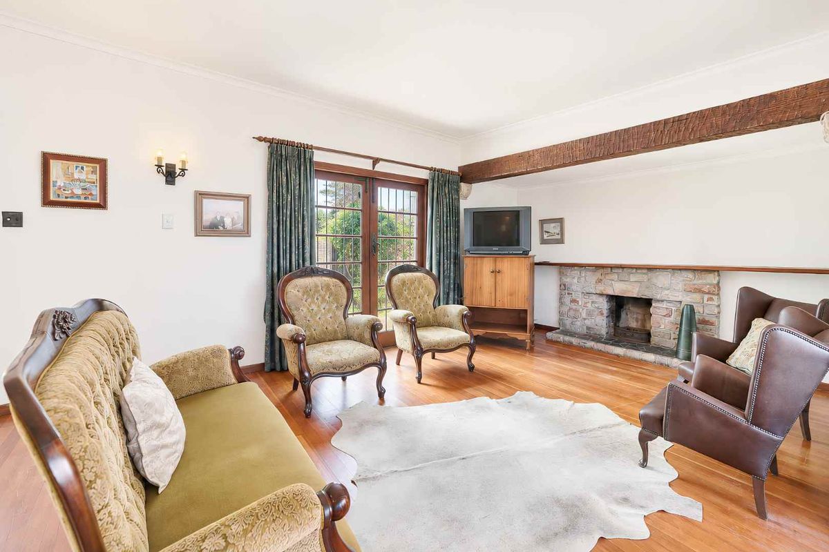 A cozy living room featuring a stone fireplace, exposed timber ceiling beam, hardwood flooring, and french doors leading to the exterior.