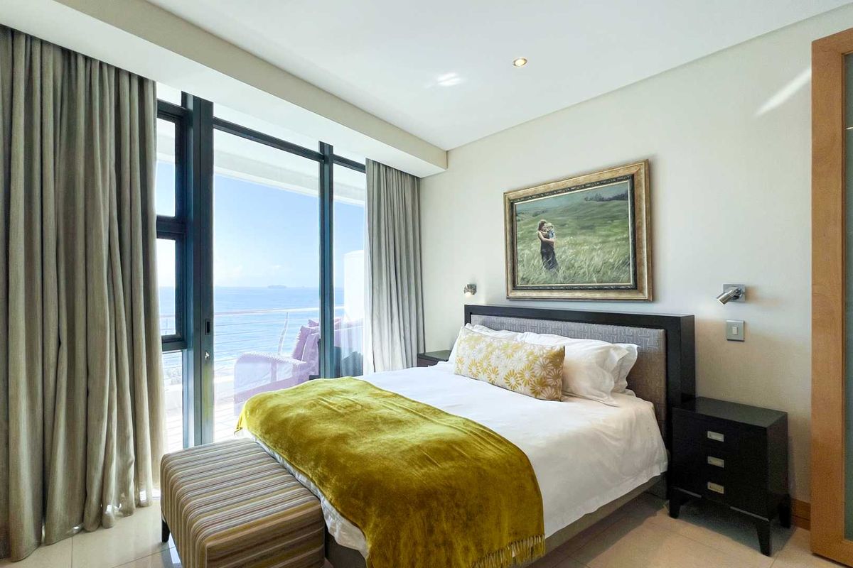 A well-maintained bedroom featuring floor-to-ceiling sliding glass doors that open to a balcony with expansive ocean views.