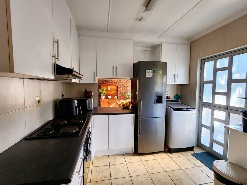 A functional kitchen featuring white cabinetry, dark countertops, an electric hob with extractor fan, and tiled flooring with direct access to the exterior.