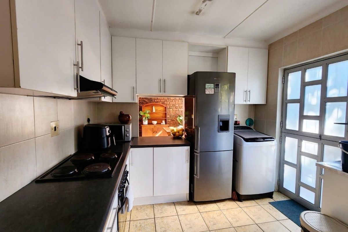 A functional kitchen featuring white cabinetry, dark countertops, an electric hob with extractor fan, and tiled flooring with direct access to the exterior.