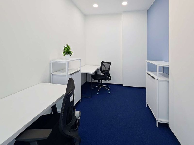 A clean, modern office space featuring recessed lighting, a bold blue accent wall, and blue carpeting, providing a professional and focused work environment.