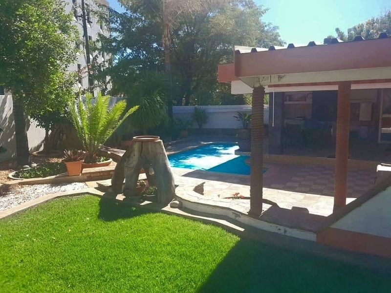 A private backyard featuring a swimming pool, a covered patio area, and a well-maintained lawn with established garden landscaping.