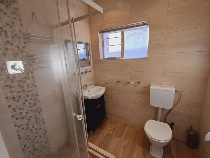 A modern bathroom featuring a glass shower enclosure with mosaic accents, a wall-mounted vanity, and neutral wall tiling.