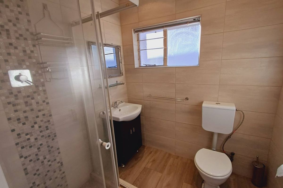 A modern bathroom featuring a glass shower enclosure with mosaic accents, a wall-mounted vanity, and neutral wall tiling.