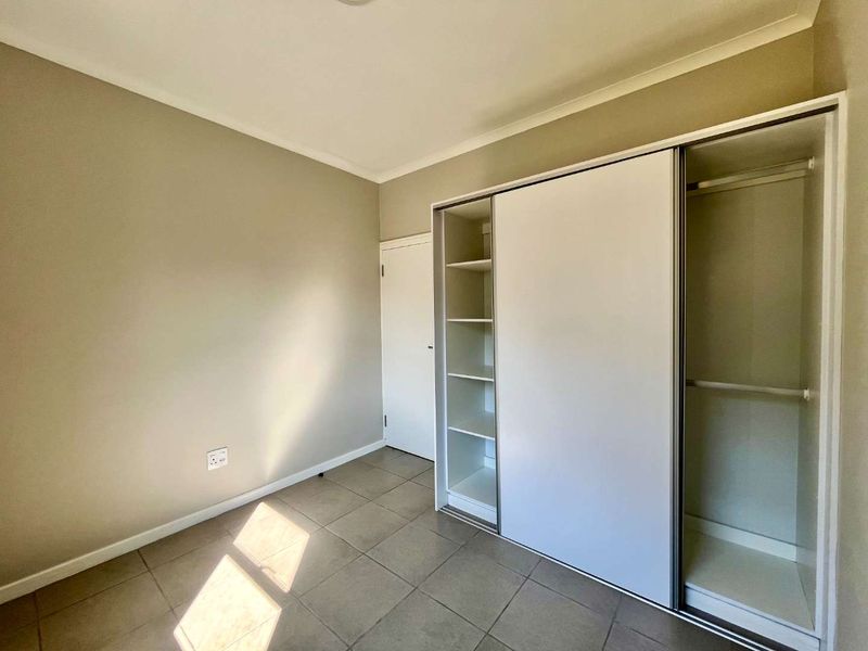 A clean, empty bedroom featuring neutral wall paint, tiled flooring, and a modern built-in sliding door wardrobe with integrated shelving.