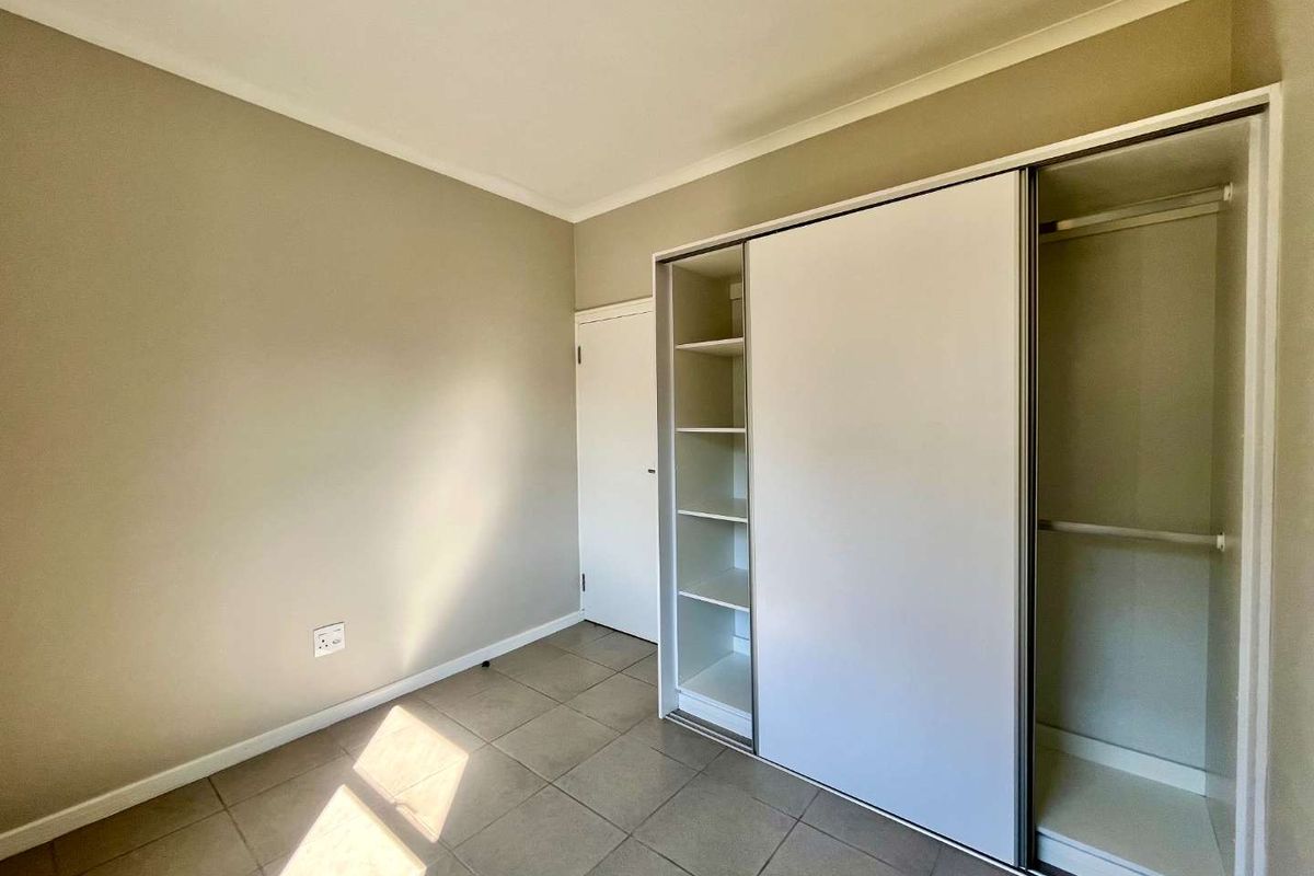 A clean, empty bedroom featuring neutral wall paint, tiled flooring, and a modern built-in sliding door wardrobe with integrated shelving.