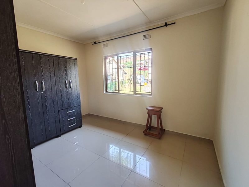 A clean, empty bedroom featuring tiled flooring, a window with security bars, and a neutral wall finish, ready for personalization.