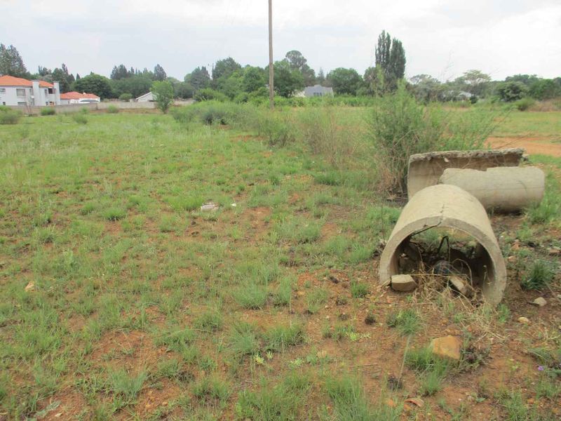 A vacant residential plot featuring natural grass cover, a utility pole, and scattered concrete drainage pipe sections.