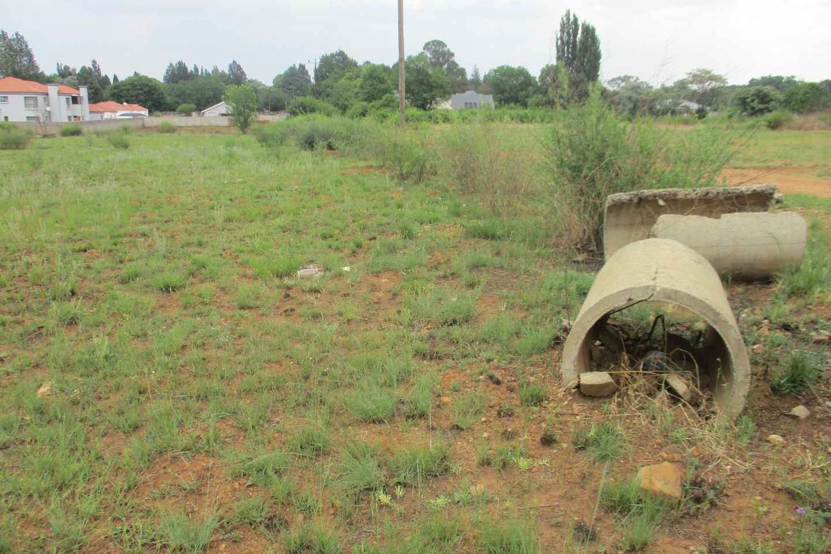 A vacant residential plot featuring natural grass cover, a utility pole, and scattered concrete drainage pipe sections.