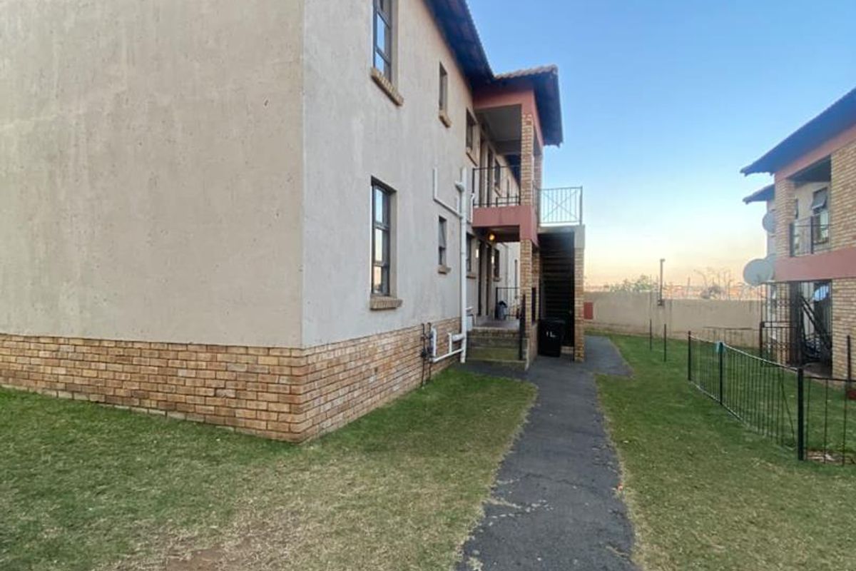 Exterior view of the townhouse complex featuring a brick and plaster facade, tiled roof, and a paved walkway leading to the building entrance.