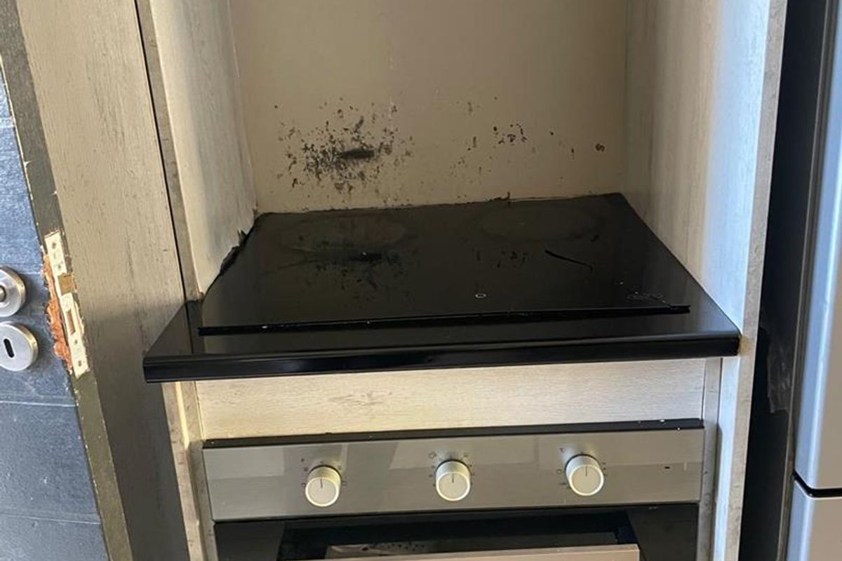A compact kitchen cooking station featuring a built-in oven and electric hob with visible wear and surface staining on the splashback area.