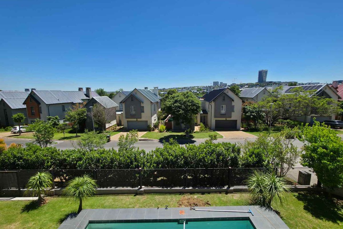 Elevated view overlooking a private swimming pool, landscaped garden, and surrounding residential estate with clear blue skies.