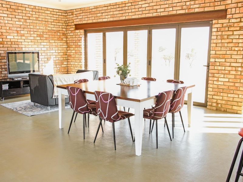 Spacious open-plan living and dining area featuring exposed brick walls, polished concrete floors, and large folding glass doors providing ample natural light.