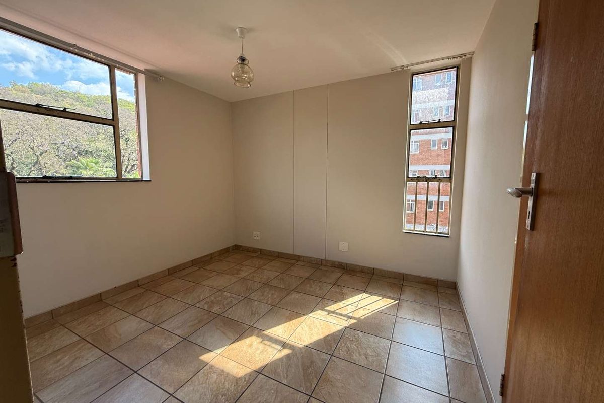 An empty bedroom featuring tiled flooring and large windows with security bars, offering natural light and a neutral backdrop for potential interior design.