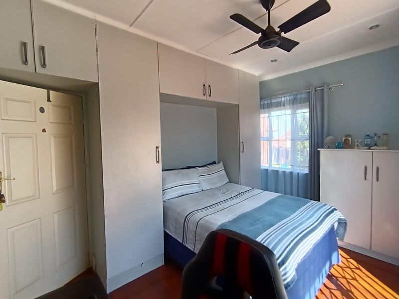 A well-maintained bedroom featuring built-in cupboards, a ceiling fan, and laminate flooring, offering a functional and comfortable living space.