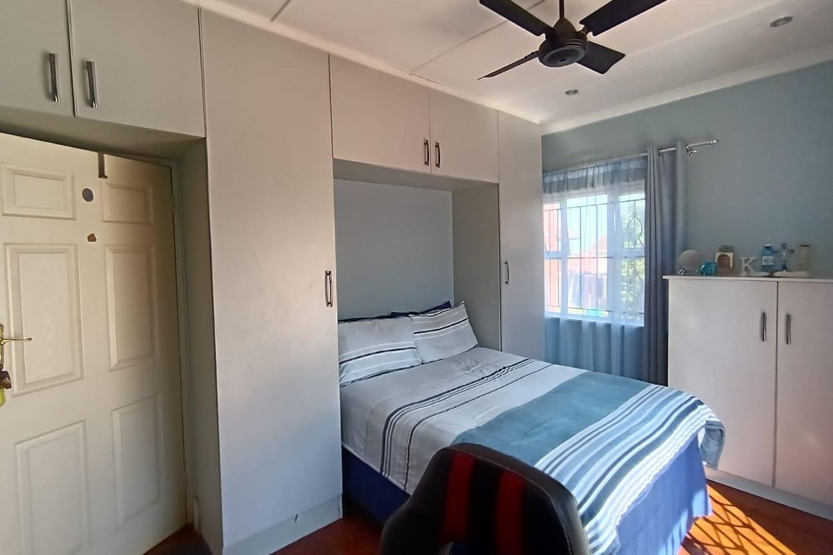 A well-maintained bedroom featuring built-in cupboards, a ceiling fan, and laminate flooring, offering a functional and comfortable living space.