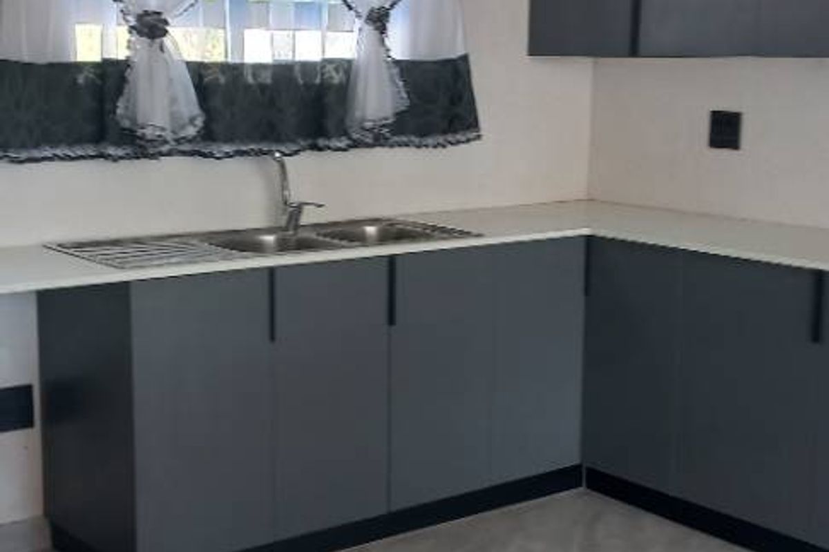 A modern kitchen featuring dark grey cabinetry, a stainless steel double sink, and light-colored countertops with tiled flooring.