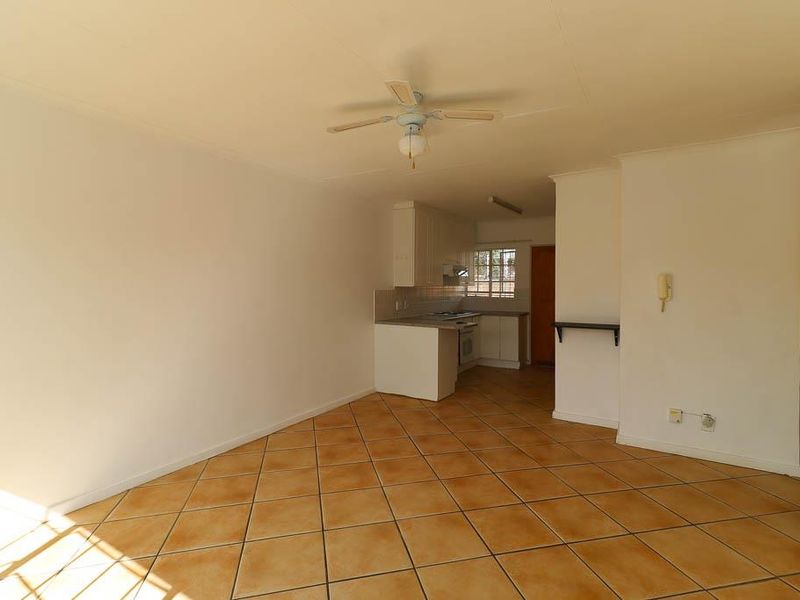 An open-plan living and kitchen area featuring tiled flooring, a ceiling fan, and functional built-in kitchen cabinetry with integrated appliances.