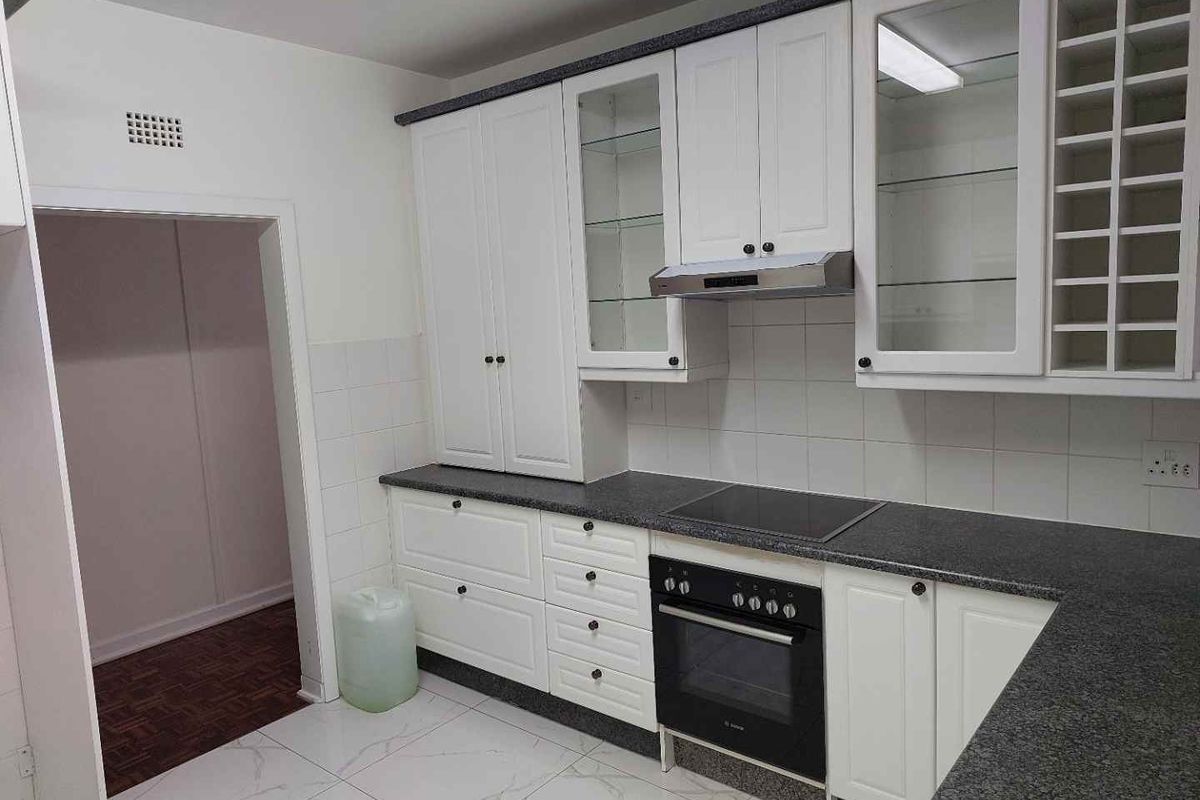 A clean, functional kitchen featuring white cabinetry, dark granite countertops, built-in oven and hob, and modern white floor tiles.
