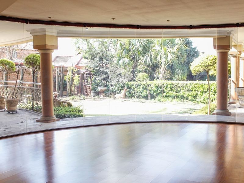 Spacious living area featuring polished hardwood floors and expansive frameless glass doors opening onto a covered patio and private garden.