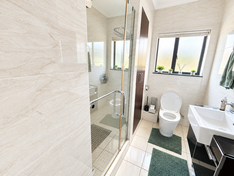 Modern bathroom featuring a glass-enclosed shower, wall-mounted toilet, and vanity basin with neutral marble-look wall tiling and tiled flooring.