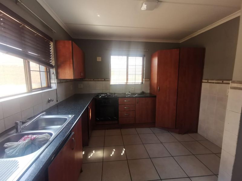 A functional kitchen featuring granite countertops, wooden cabinetry, a built-in oven and hob, and tiled flooring with ample natural light.