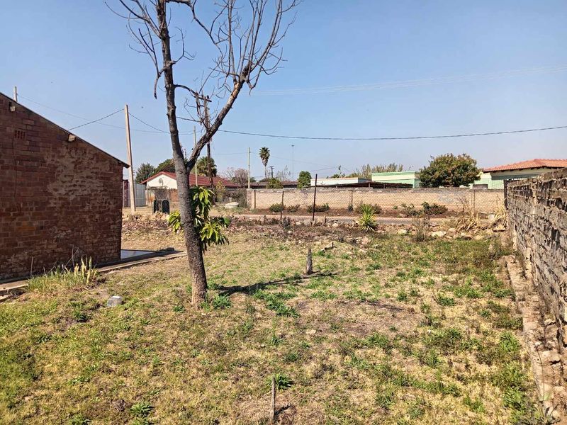 A spacious, unmaintained rear garden area featuring a brick boundary wall and exposed brick exterior wall, offering significant potential for landscaping and outdoor development.