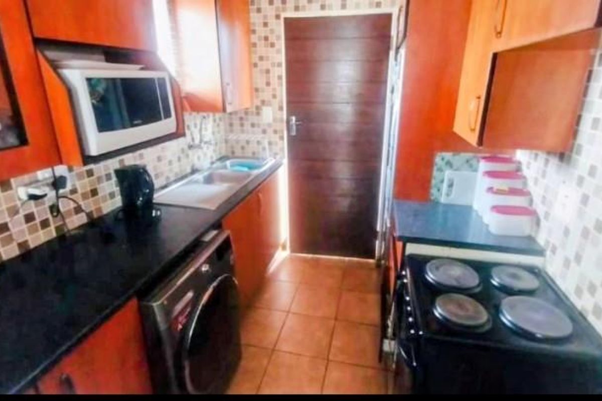 A compact kitchen featuring wooden cabinetry, mosaic tile backsplash, dark countertops, and built-in appliances including an electric stove and microwave.