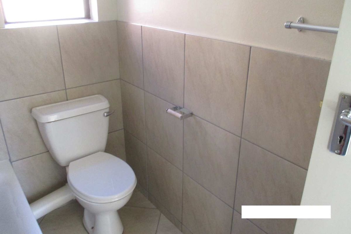 A functional bathroom featuring neutral wall and floor tiling, a standard toilet, and fixed bathroom accessories.