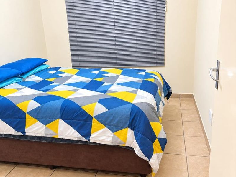 A functional bedroom featuring neutral wall tones, tiled flooring, and a window fitted with grey venetian blinds.